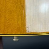 Close-up of a wooden surface with a glossy finish, showing a vertical seam between a warm golden-brown section and a lighter cream section, with a dark blue background below.