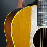Close-up of an acoustic guitar body showing the natural wood finish, sound hole, rosette, and part of the fretboard against a dark background.