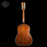 The back of a vintage acoustic guitar with a rich brown wooden body and neck, shown against a solid black background with a Tone Shop watermark in the top left corner.