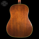 The back of a wooden acoustic guitar, showing a rich brown wood grain finish and a thin gold-toned edge trim, set against a solid black background with a Tone Shop watermark in the top left corner.