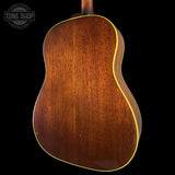 The back of an acoustic guitar with a rich, warm brown wood finish and a thin gold-toned binding edge, shown against a solid black background with a Tone Shop watermark in the upper left.