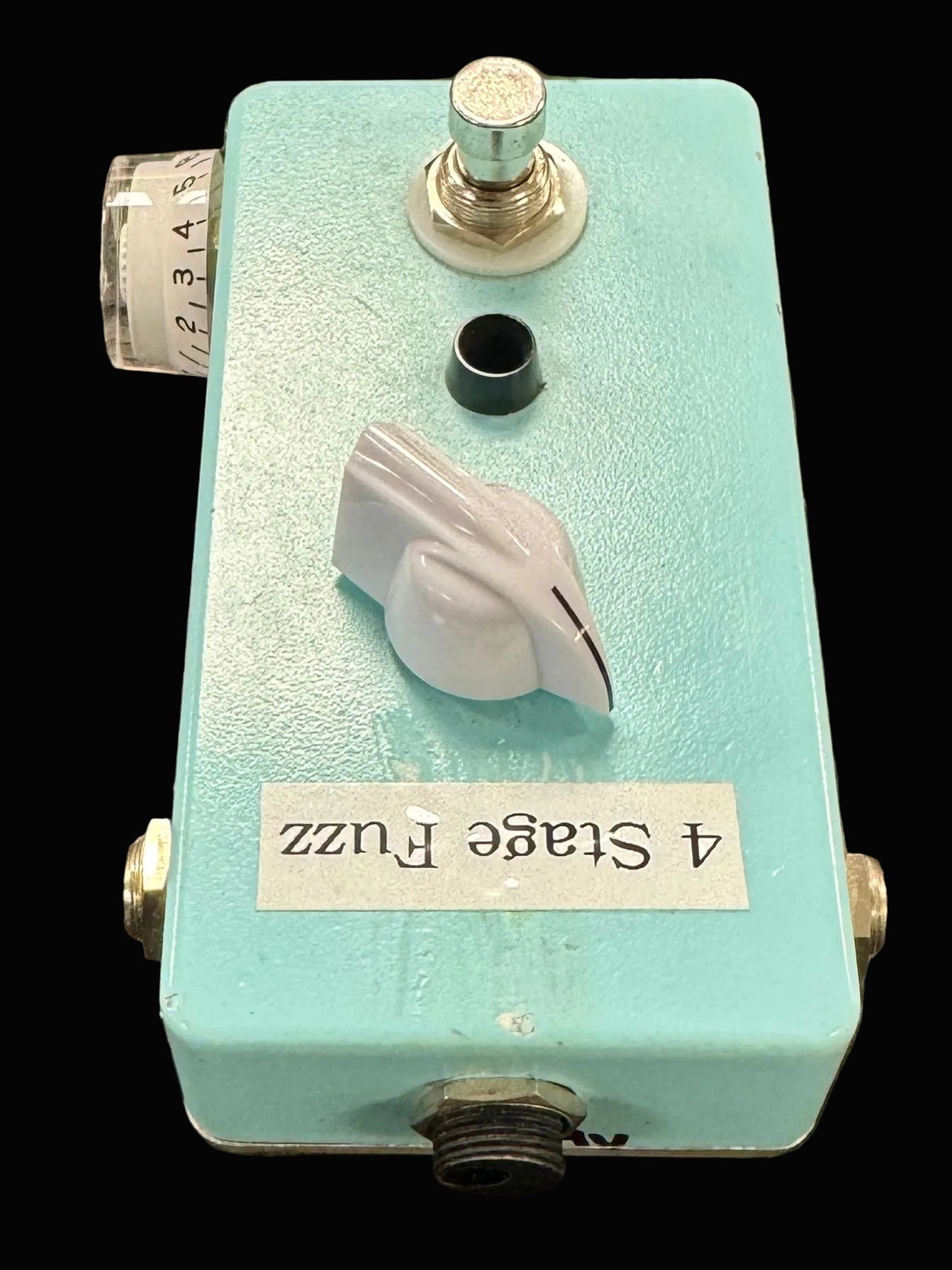 Turquoise guitar effects pedal with '4 Stage Fuzz' label on a textured surface