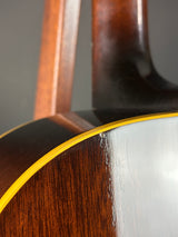 Close-up detail of an acoustic guitar body showing the glossy dark brown wood grain, a bright yellow binding edge, and a light gray backplate.