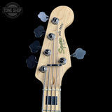Close-up of a Squier Jazz Bass headstock with a natural maple wood finish, four silver tuning pegs, and a black background. A Tone Shop watermark is visible in the top-left corner.