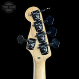Close-up of the headstock of a bass guitar with six black four-lobed tuning pegs and a light natural wood finish, shown against a solid black background.