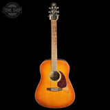 A vintage acoustic guitar with a natural sunburst finish, shown against a solid black background. A Tone Shop watermark is visible in the top-left corner.