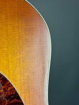 Close-up of an acoustic guitar body showing the warm brown wood grain and a dark gray background.