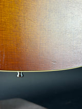 Close-up of a guitar body showing a sunburst gradient from dark brown to warm amber wood grain, with a small silver hardware piece near the edge.