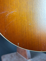 Close-up of a wooden surface with a warm brown finish and visible scratches, showing part of a curved edge and a dark background.