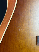 Close-up of a wooden acoustic guitar body showing the natural wood grain, a small scratch on the surface, and part of the soundhole rim.
