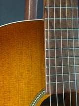 Close-up detail of an acoustic guitar showing the dark wood fretboard with metal strings and the warm golden-brown wood body.