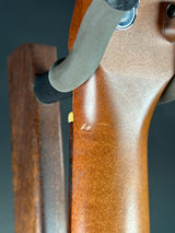 Close-up of a wooden rifle stock with a brown wood finish, showing a metal lever and dark background.