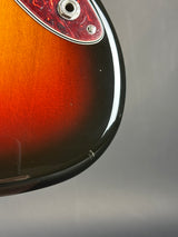 Close-up of the upper bout corner of an electric guitar body, showing a glossy sunburst finish that transitions from amber-orange to black, with part of the red marbled pickguard and silver hardware visible.
