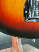 Close-up of a sunburst electric guitar body showing the transition from bright orange to dark brown and black, with part of the chrome hardware and pickguard visible.