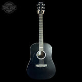 A black acoustic guitar with a glossy finish, shown vertically against a solid black background. A circular 'TONE SHOP' watermark is visible in the top-left corner.