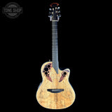 A double-cutaway acoustic guitar with a natural wood body showing prominent grain patterns, dark fingerboard, and decorative circular cutouts on the upper bout, set against a solid black background with a Tone Shop logo in the top-left corner.