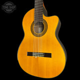 A classical-cutaway acoustic guitar with a natural golden-yellow wood finish, shown against a solid black background. The brand logo 'TONE SHOP' is visible as an overlay in the top-left corner.