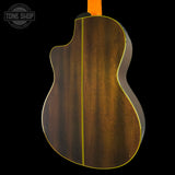 The back of an acoustic guitar with a dark brown wood finish and a bright yellow binding, shown against a solid black background. A Tone Shop watermark is visible in the top left corner.
