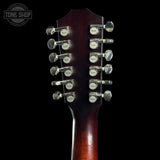 Close-up of the headstock of a double-necked acoustic guitar, showing twelve tuning pegs with Tone Shop branding, set against a solid black background.