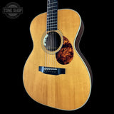 A close-up studio shot of an acoustic guitar body and upper neck against a black background, with a Tone Shop watermark in the top-left corner.