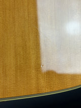 Close-up detail of a guitar body showing the natural wood grain finish, a white gloss reflection on the upper section, and the edge of the instrument with a black binding strip.