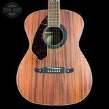An acoustic guitar with a rich reddish-brown wood grain finish, featuring a dark tortoiseshell pickguard and bridge, set against a solid black background with a Tone Shop watermark in the top left corner.