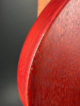 Close-up of a curved wooden surface with a reddish-brown wood grain finish, showing the edge and texture in detail against a dark background.