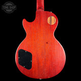 The back of a classic electric guitar with a glossy red cherry wood finish, featuring a black pickguard and a circular wood inlay near the upper bout, shown against a solid black background.