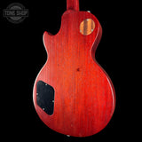 The rear view of an electric guitar with a glossy red cherry finish, featuring a black pickguard and a circular wood grain inlay near the upper back, shown against a solid black background.