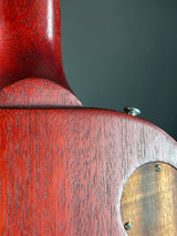 Close-up detail of a reddish-brown wooden guitar body showing the wood grain, a metal screw, and part of a circular soundhole cover with screws.