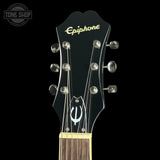 Close-up of the headstock of an Epiphone electric guitar against a black background, showing the gold Epiphone logo and silver tuning pegs.
