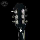 Close-up rear view of a black electric guitar headstock with six silver tuning pegs and a glossy finish, shown against a black background with a Tone Shop watermark in the upper left.