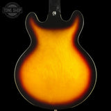 Close-up of the back of an electric guitar body with a classic sunburst finish, showing a bright amber-yellow center fading to black around the edges, set against a solid black background.