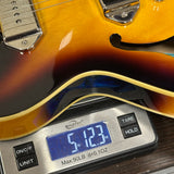 Close-up of a guitar body resting on a digital scale showing a weight of 5.123 oz.