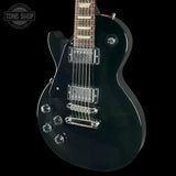 A black electric guitar with chrome hardware, shown from a side angle against a black background. A 'TONE SHOP' watermark is visible in the top-left corner.