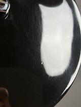 Close-up of a glossy black curved surface with a large white reflection, showing fine scratches and dust on the finish.