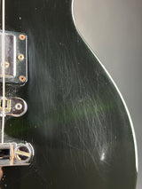 Close-up of a black electric guitar body showing the glossy finish, visible scratch marks, and chrome hardware near the pickups.