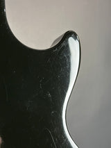 Close-up of a glossy black guitar body with visible scratches and scuffs on a neutral gray background.