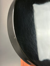 Close-up of a glossy black circular object with visible scratches and a white reflective area near the top, photographed against a light gray surface.
