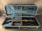 Black electric guitar in an open gray guitar case on a neutral background