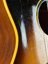 Close-up of a guitar body showing the glossy dark top, natural wood lower section, and a yellow binding line.