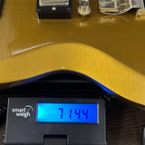 A close-up of a gold metallic electric guitar body resting on a digital smart weigh scale displaying 714.4 oz.