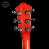Close-up of a guitar headstock with six silver tuning pegs and a glossy reddish-orange wood finish, shown against a black background with a Tone Shop watermark in the top left.