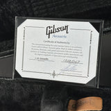 A Gibson Acoustic J-45 Granadillo authenticity certificate card in a clear protective sleeve, displayed on a black velvet surface with a small tan Gibson logo tag visible at the bottom right.