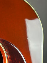Close-up of an acoustic guitar body showing the glossy brown wood finish, sound hole rosette, and a thin cream-colored binding edge against a dark background.
