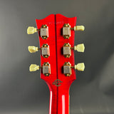 Close-up of a red guitar headstock with tuning pegs on a gray background