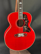 Red acoustic guitar with a dark brown pickguard on a black background
