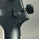Close-up of a black instrument headstock with a visible PRS logo on a tuning peg and a black tuning key, against a plain gray background.