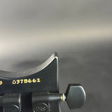 Close-up of a black BRS guitar headstock showing the top edge, gold serial number 0378662, and part of the tuning pegs against a blurred gray background.