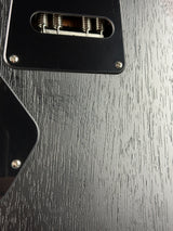 Close-up of a black guitar body with a visible single-coil pickup, metal springs, and a dark woodgrain finish.